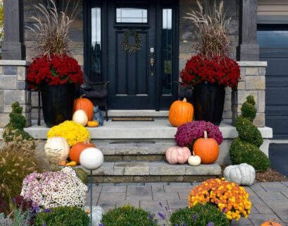 Fall porch decorating ideas with colorful mums, pumpkins, and potted plants arranged on front steps.