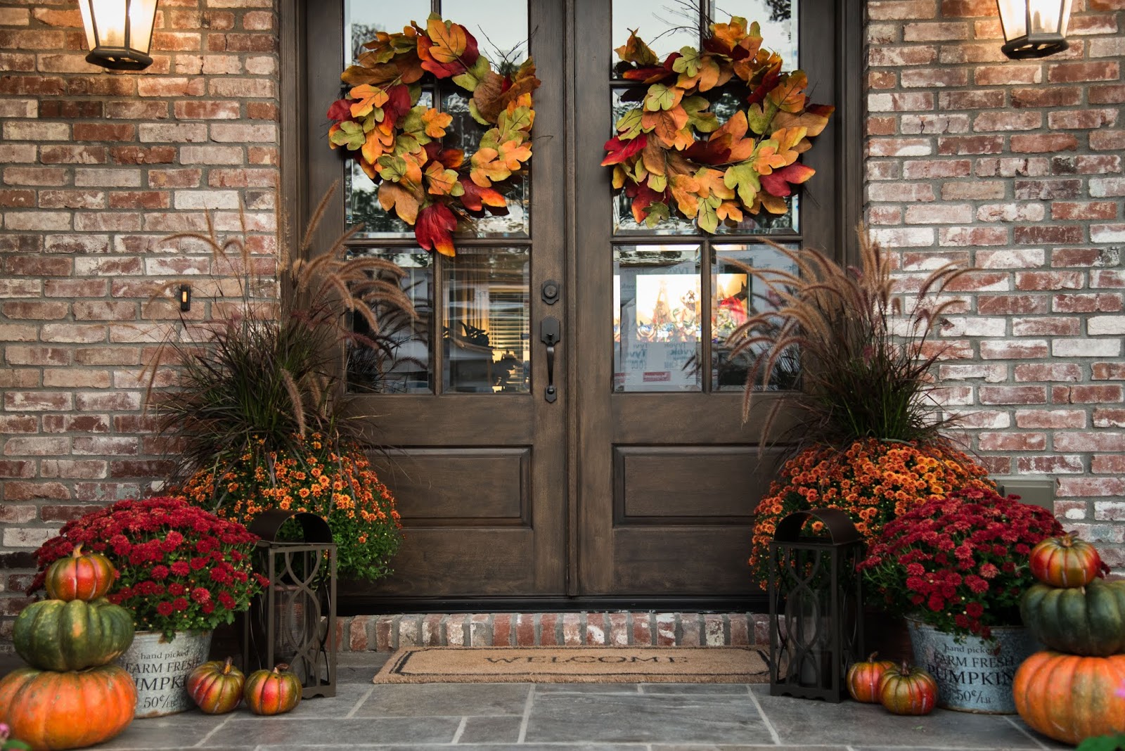 Fall front porch with double doors, pumpkins, mums, and colorful autumn wreaths