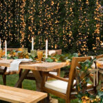 Outdoor dining table decorated with greenery, candles, and warm string lights for an elegant backyard dinner party.