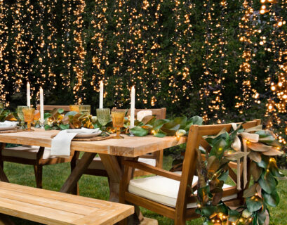Outdoor dining table decorated with greenery, candles, and warm string lights for an elegant backyard dinner party.