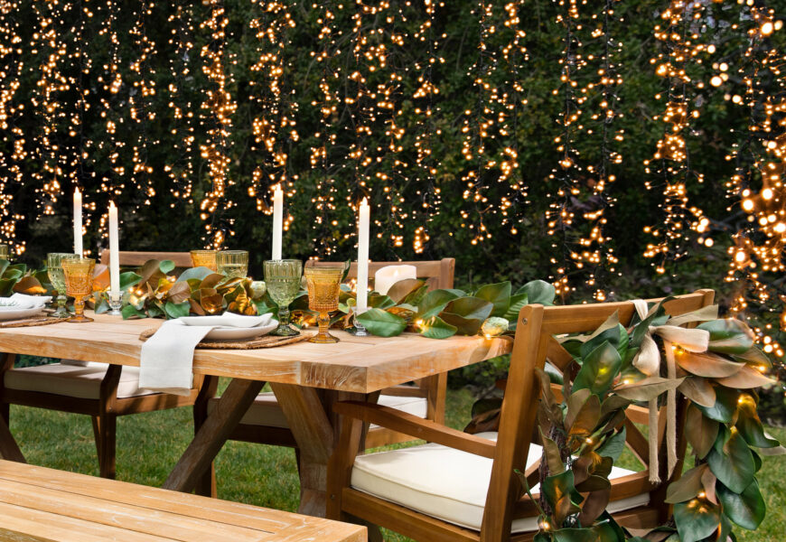 Outdoor dining table decorated with greenery, candles, and warm string lights for an elegant backyard dinner party.