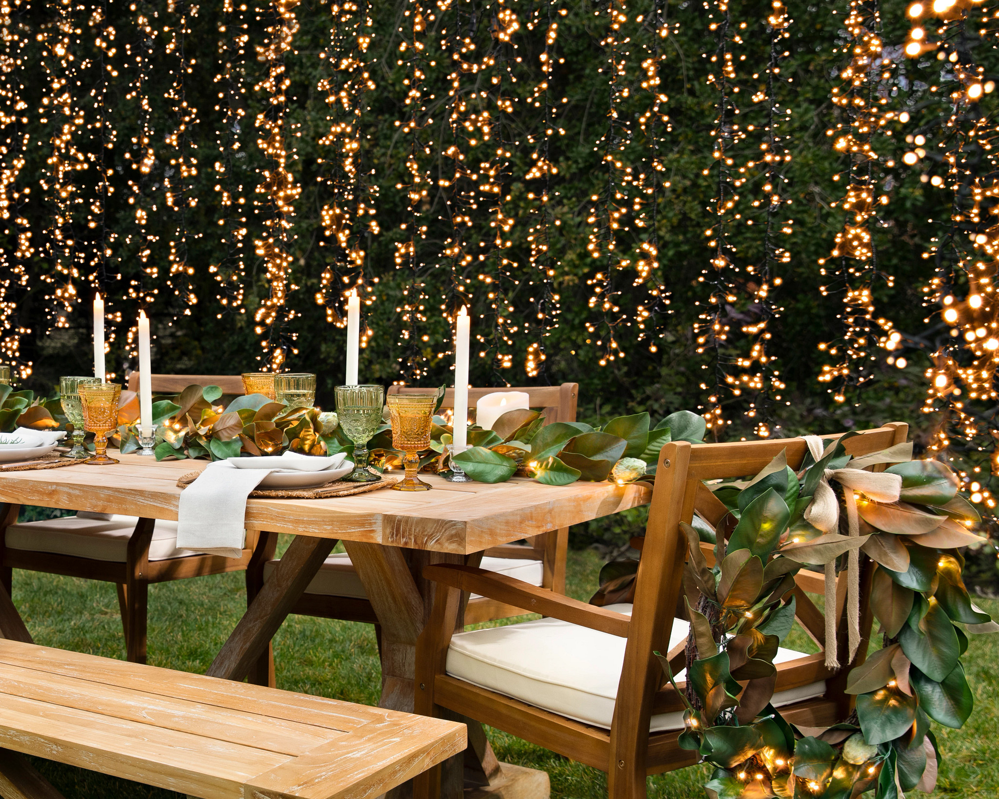 Outdoor dining table decorated with greenery, candles, and warm string lights for an elegant backyard dinner party.