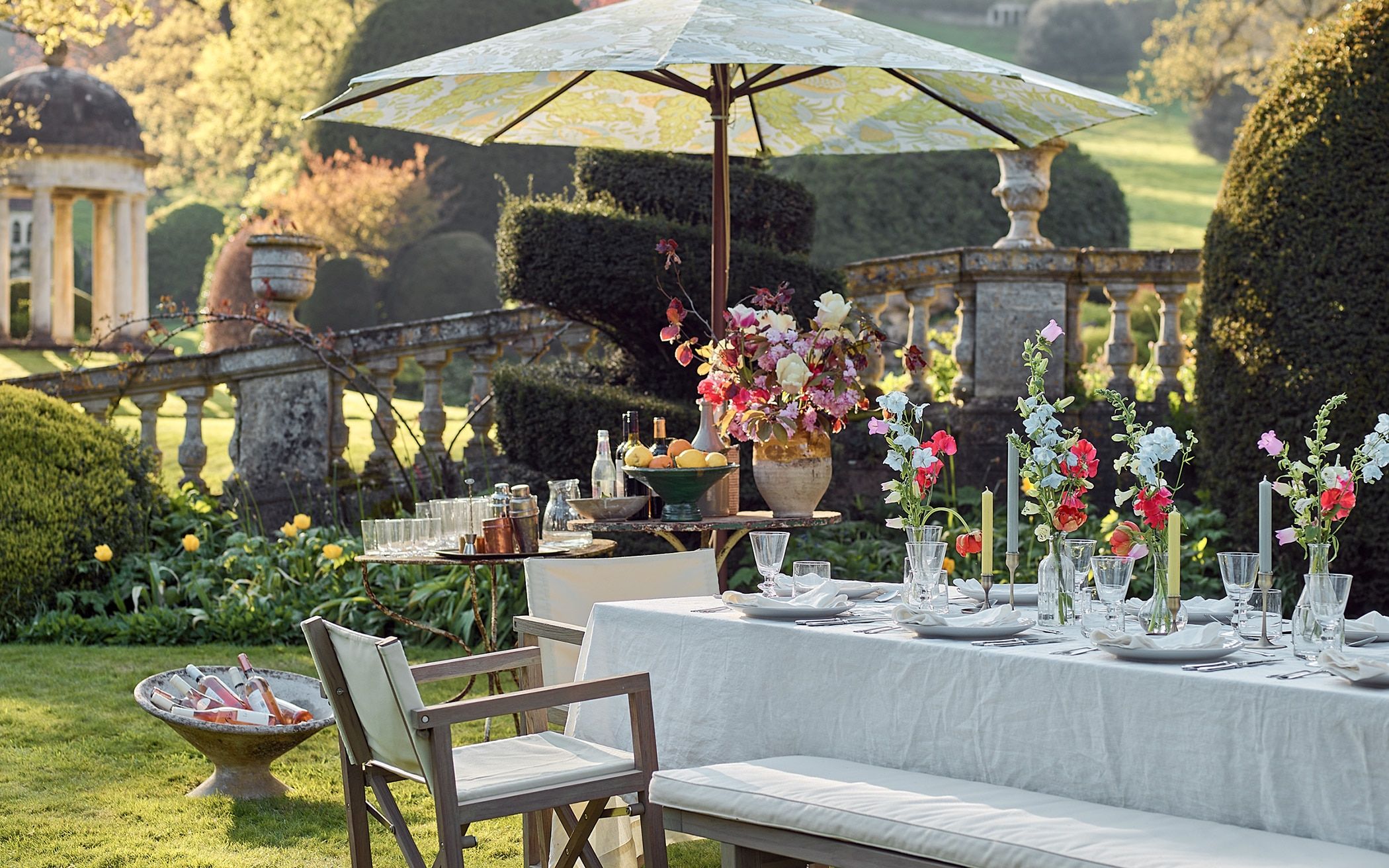 Elegant outdoor table decoration Ideas with fresh flowers, candles, and stylish tableware under a patio umbrella.