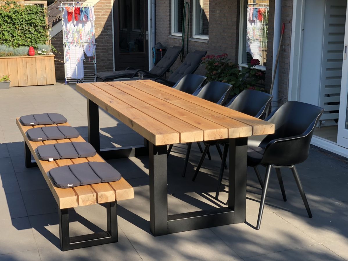Modern outdoor dining table with wooden top and black metal frame arranged on a stylish patio.