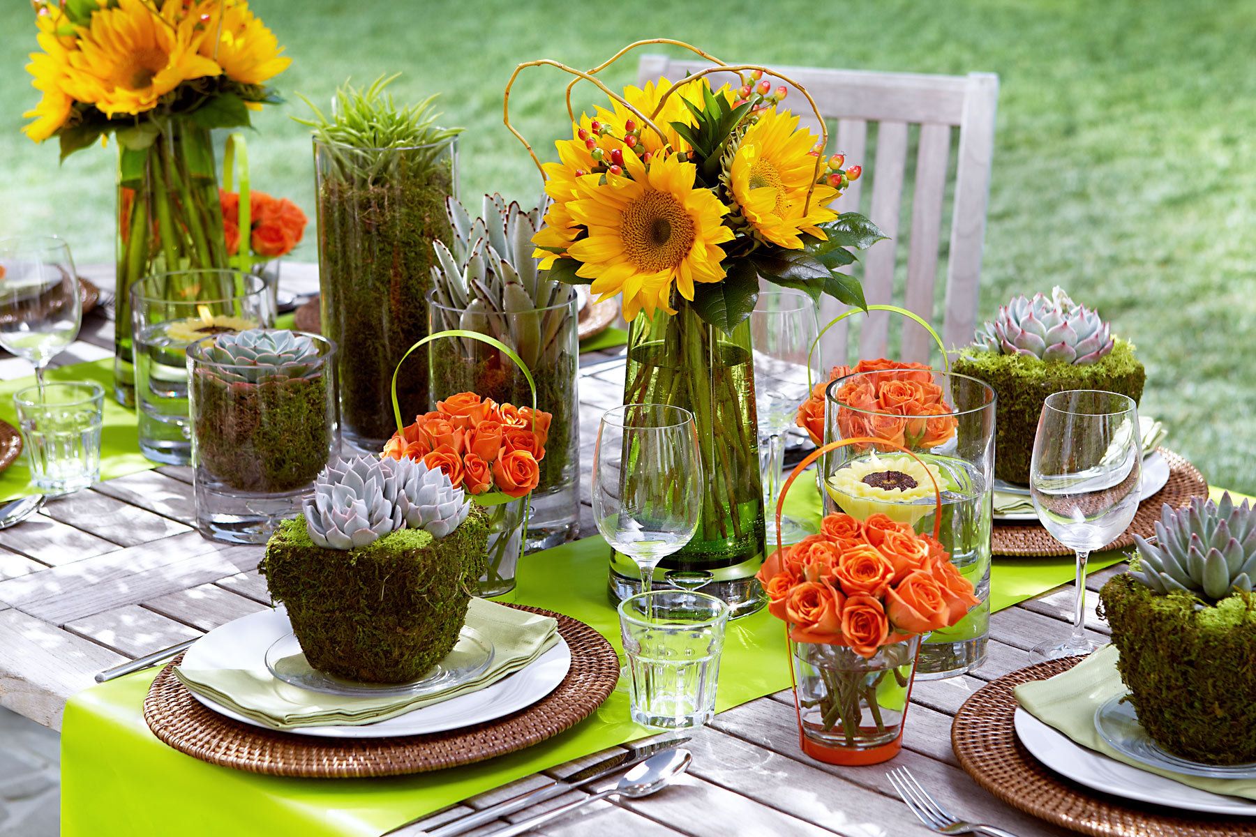Outdoor table decorated with sunflowers, orange floral arrangements, and green place settings for a vibrant dining experience.