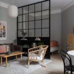 Modern apartment living room with black framed glass divider separating spaces in an open-plan layout.