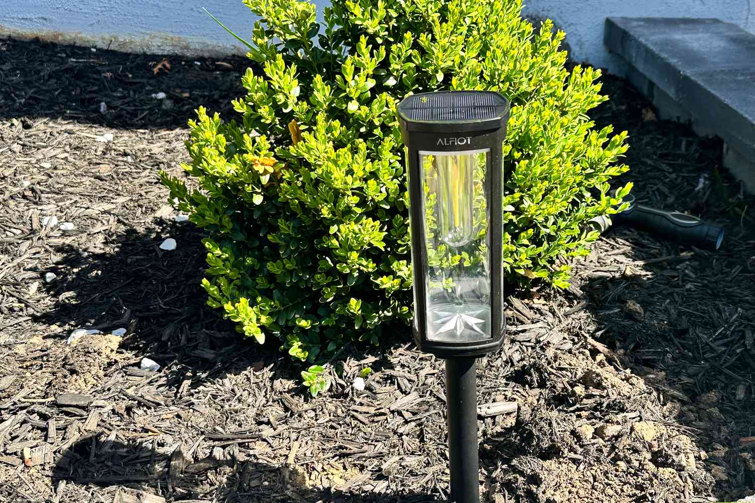 Solar powered pathway light installed in garden soil next to green bush