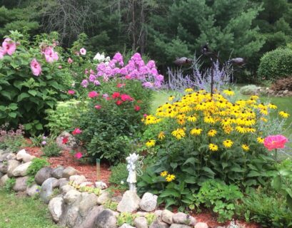 Bright perennial flower garden in Michigan with blooming flowers, rocks, and healthy green landscaping.