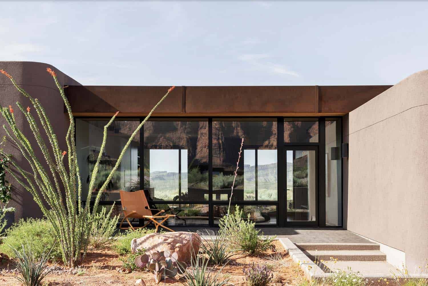Modern desert home exterior with glass walls, minimalist architecture, and natural landscape surroundings