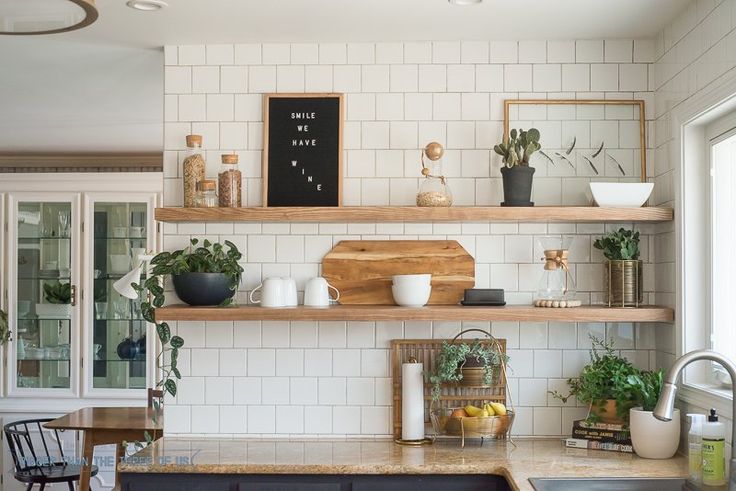 Bright kitchen with open shelf decor, white subway tiles, greenery, and wooden kitchen accessories.