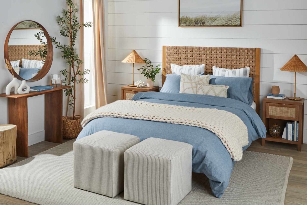 Elegant coastal bedroom with wicker accents, blue bedding, warm wood furniture, and modern beach house decor.