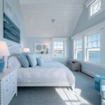 Modern coastal bedroom with panoramic ocean views, white walls, and light blue beach-inspired decor.