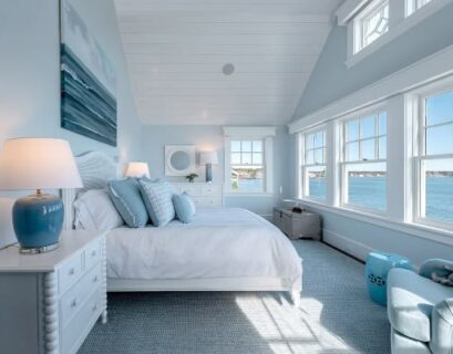 Modern coastal bedroom with panoramic ocean views, white walls, and light blue beach-inspired decor.