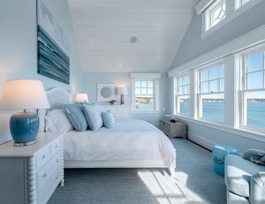 Modern coastal bedroom with panoramic ocean views, white walls, and light blue beach-inspired decor.