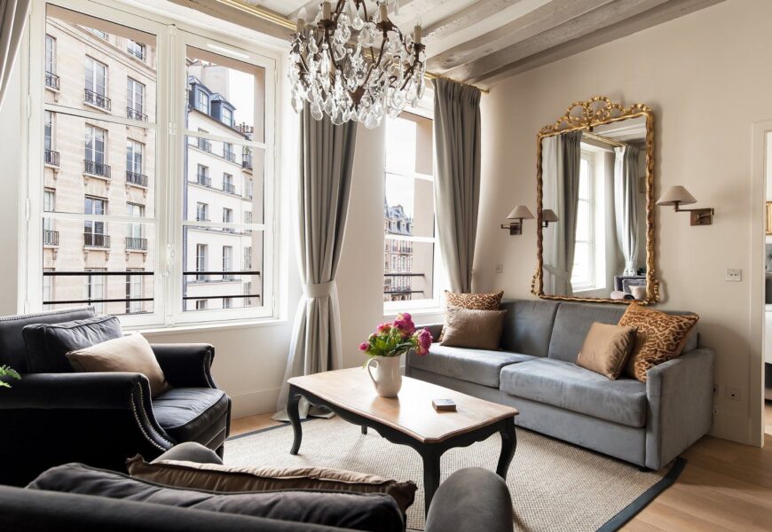 Chic Parisian apartment living room with tall windows, neutral furniture, and luxurious French interior styling.