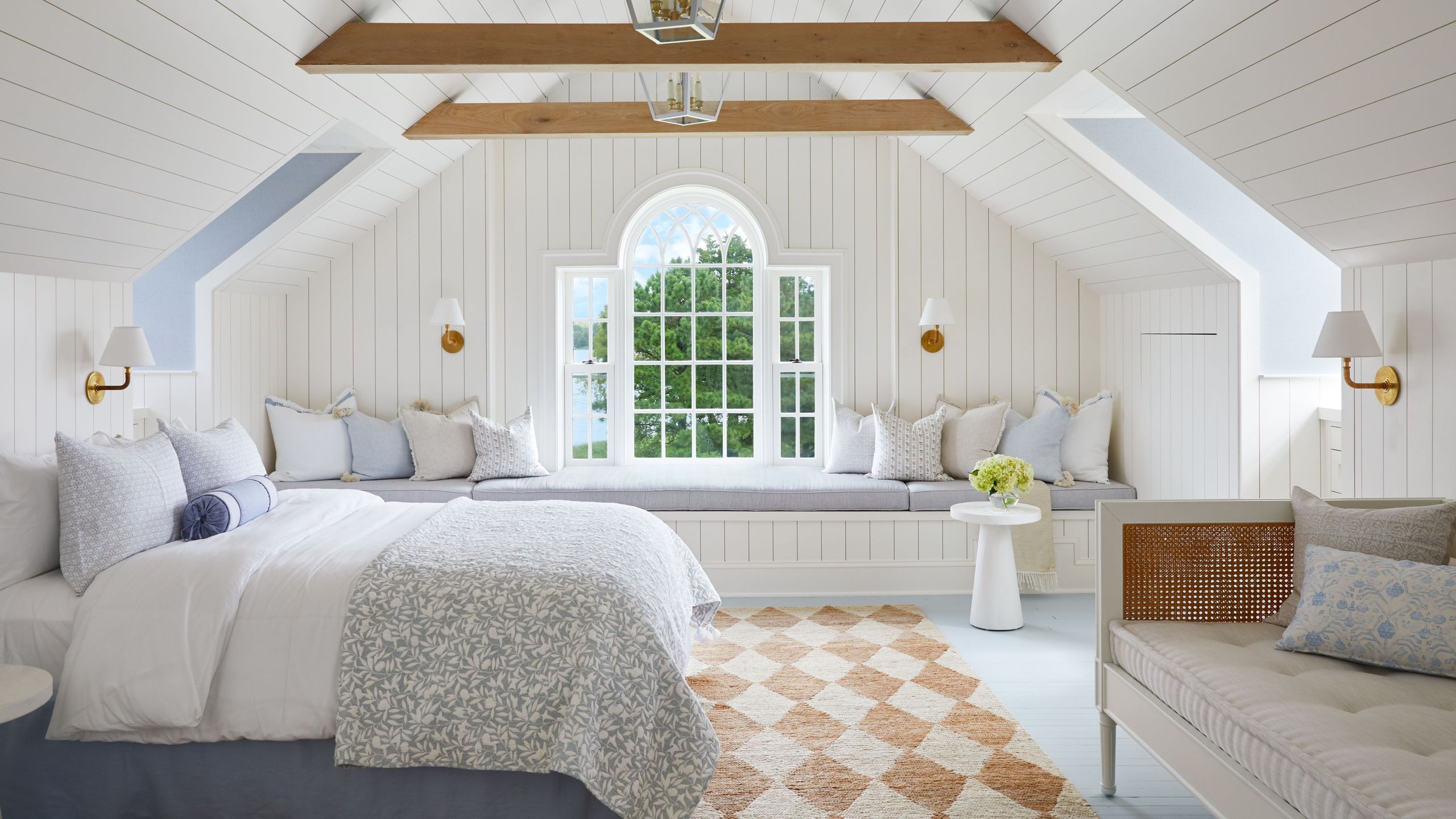 White cottagecore bedroom with arched window, wooden beams and cozy bedding