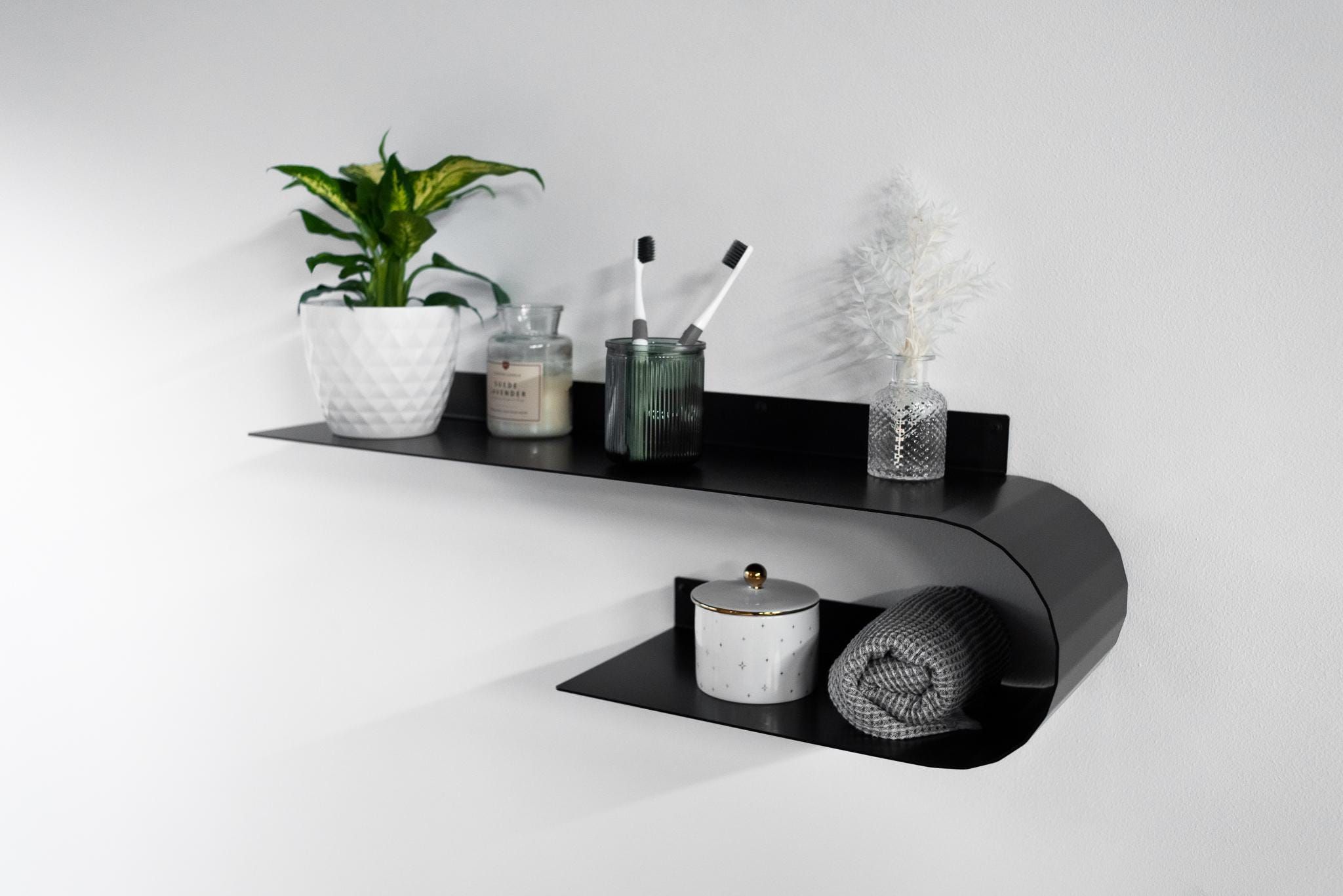 Black bathroom floating shelf with plants, jars, and modern minimalist decor