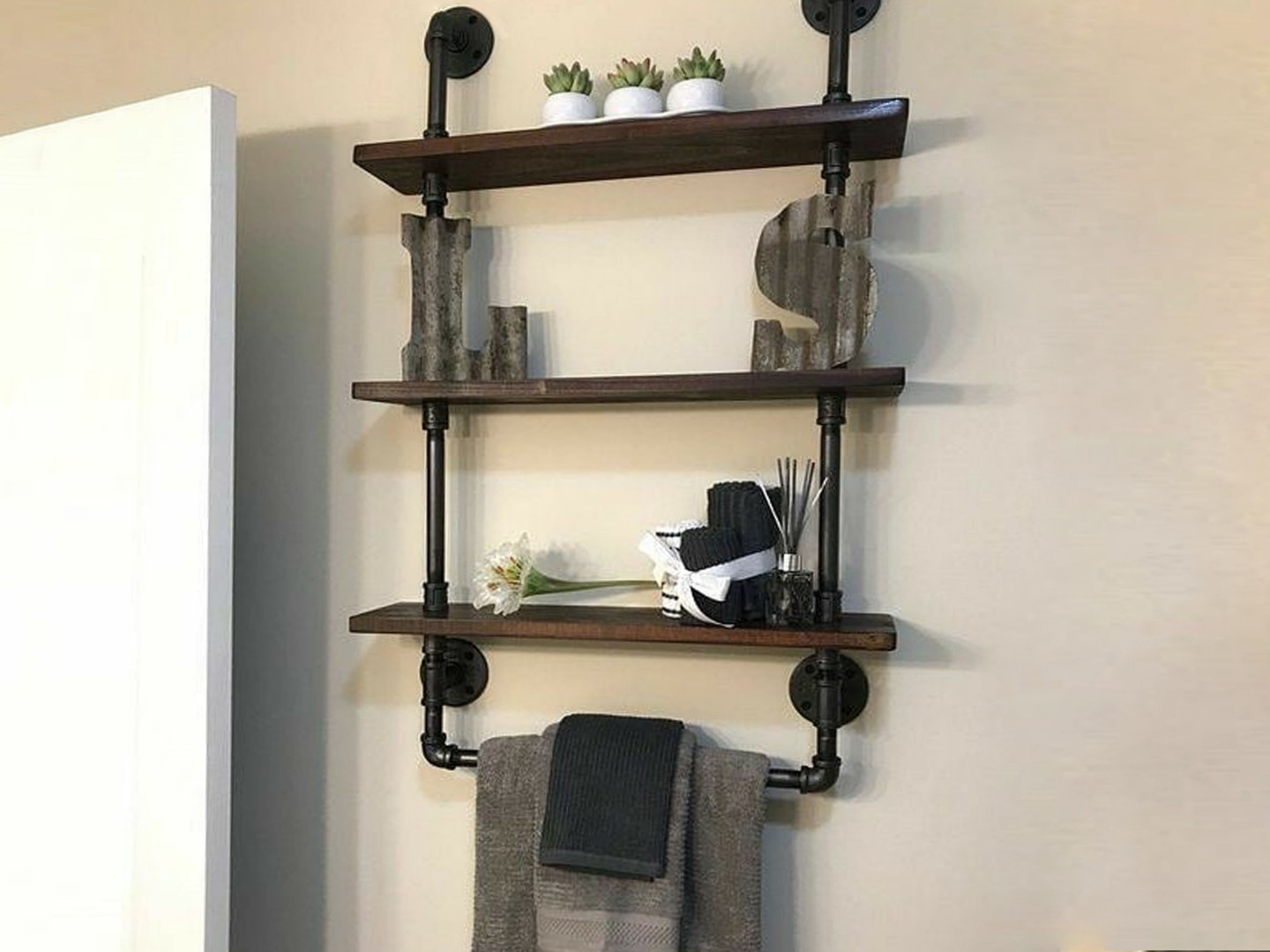 Industrial bathroom wall shelf with black metal brackets, towels, and decorative items